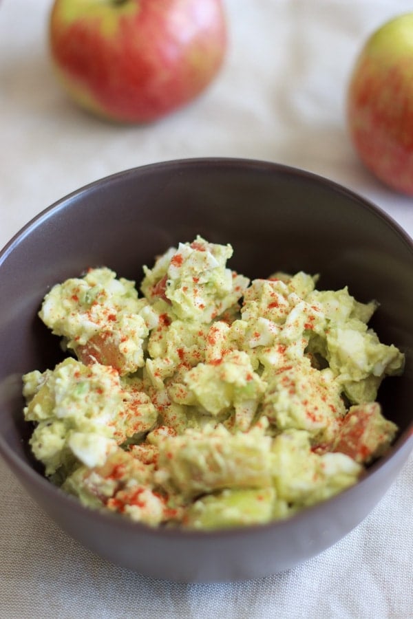 Apple avocado egg salad in brown bowl with apples in background