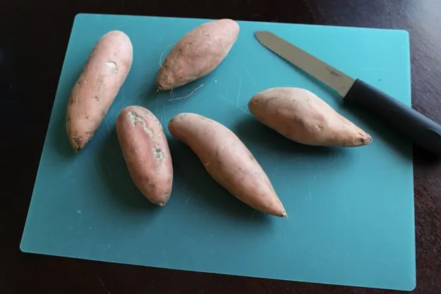 5 ssweet potatoes on blue plastic cutting board with knife