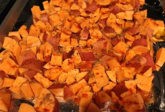 chopped sweet potatoes on aluminum foil lined baking sweet drizzled in olive oil and spices