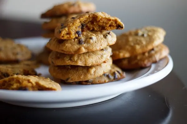 Pumpkin oatmeal chocolate chip cookies stacked on a white plate with a bite taken out of one
