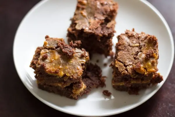 3 pumpkin cheesecake brownies on a white plate