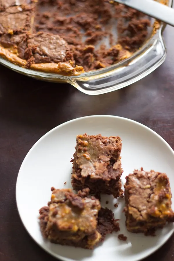 3 pumpkin cheesecake brownies on a white plate with rest in background