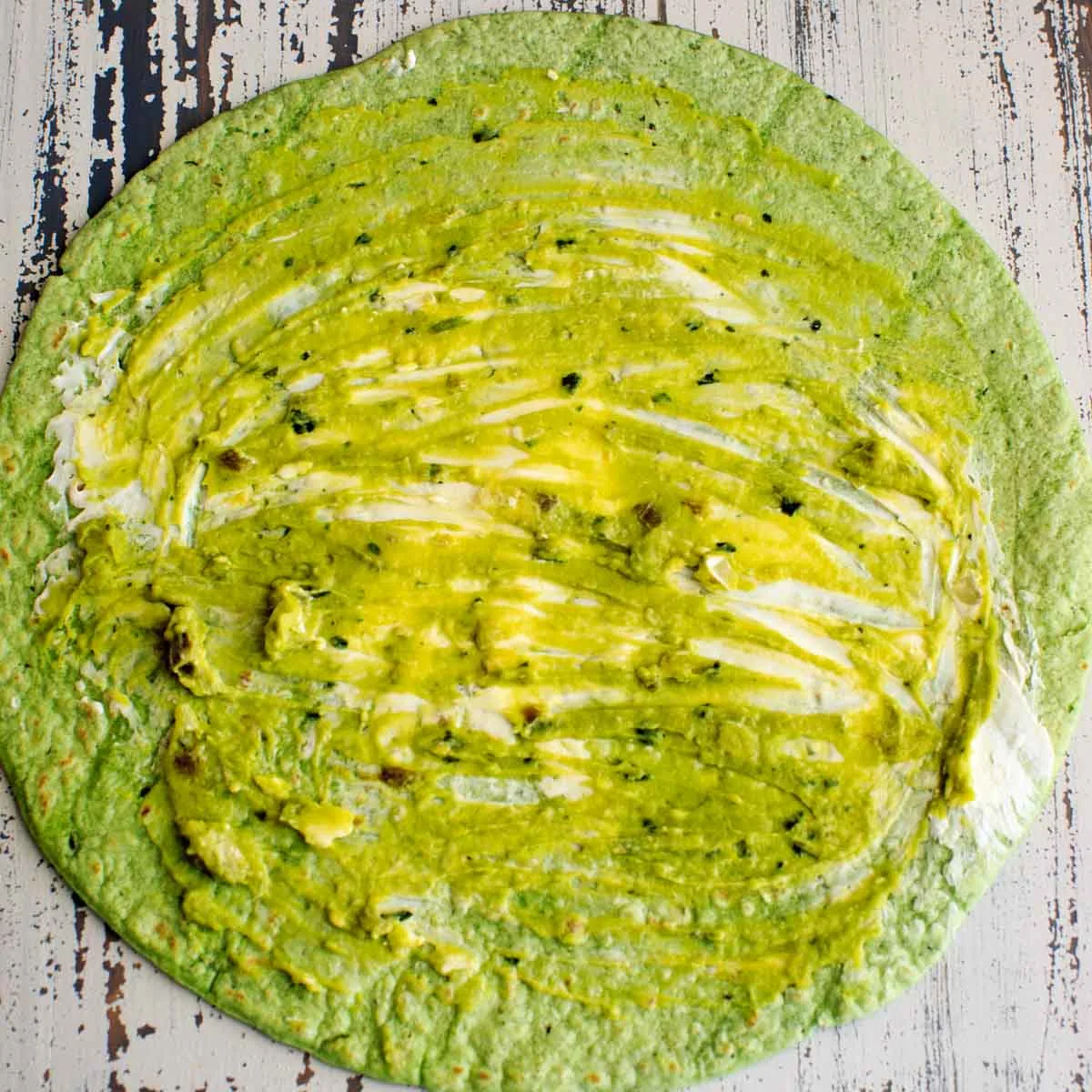 guacamole and cream cheese spread on green tortilla