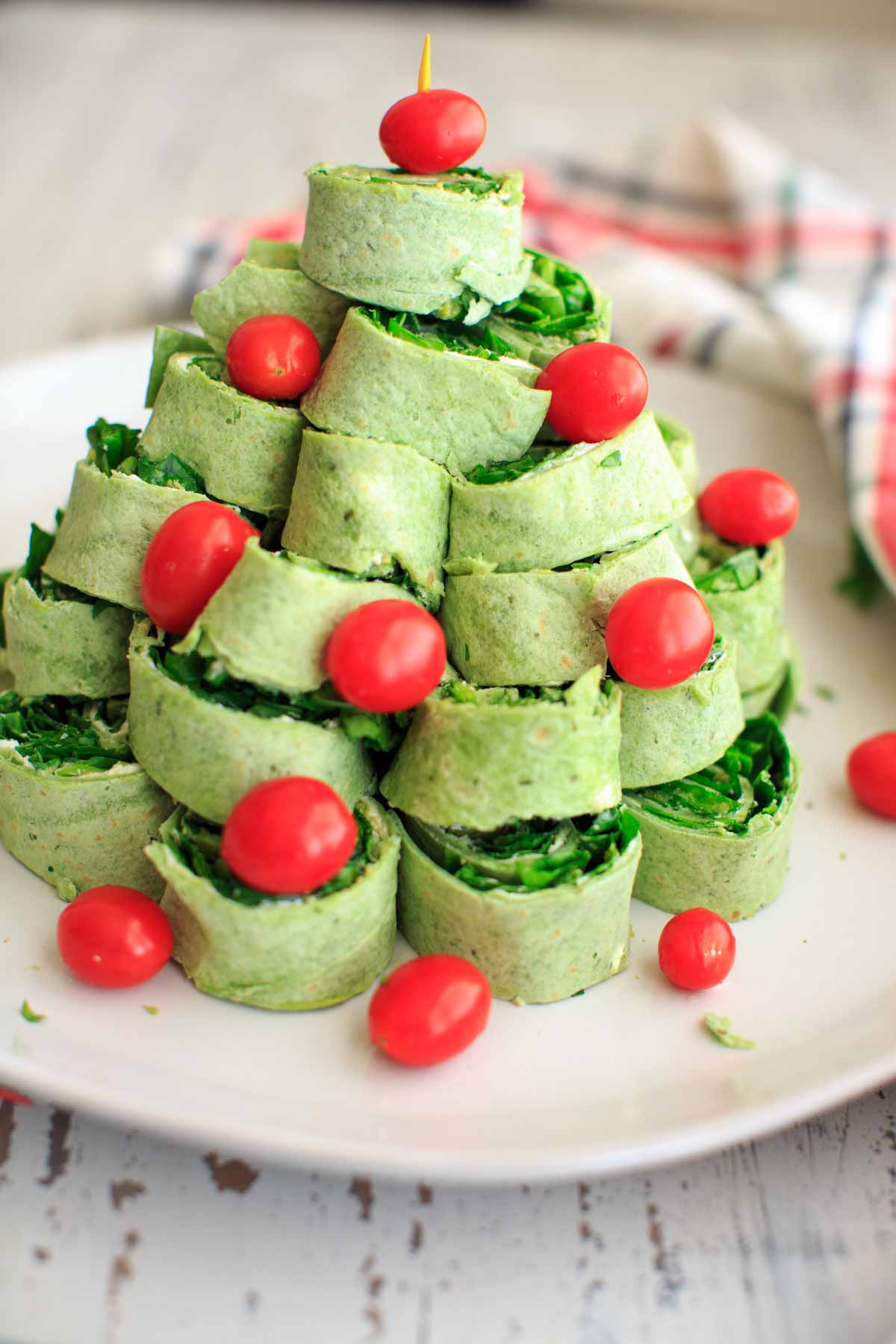 green spinach tortilla pinwheels stacked to make a christmas tree with tomatoes for ornaments