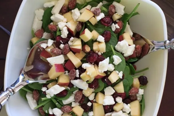 Spinach salad with apple, feta, dried cranberries and honey almonds in large salad bowl with serving spoons