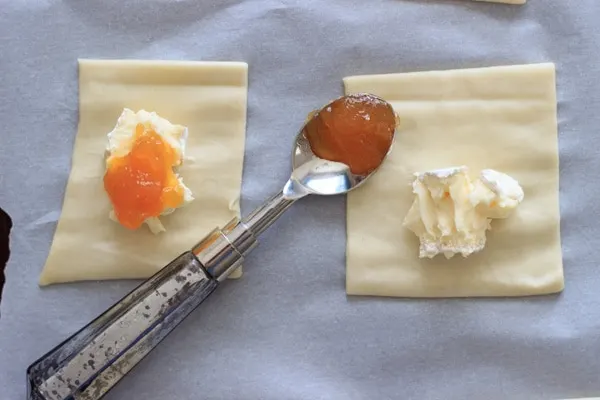spoon with apricot jam next to baked brie on puff pastry square