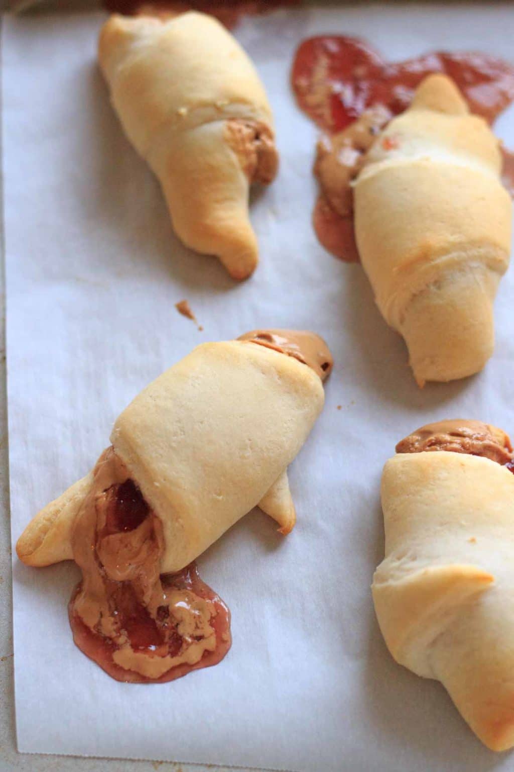 Peanut butter and jelly wraps with filling oozing out on parchment paper