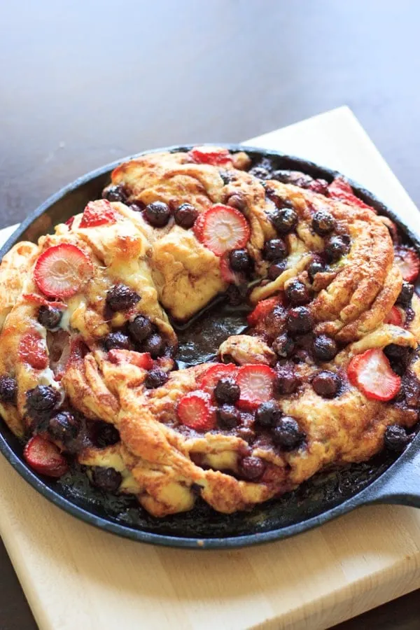 Berries swirl cinnamon bread on cast iron skillet sitting on wooden cutting board