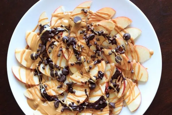 apple nachos with peanut butter and chocolate drizzle on white plate