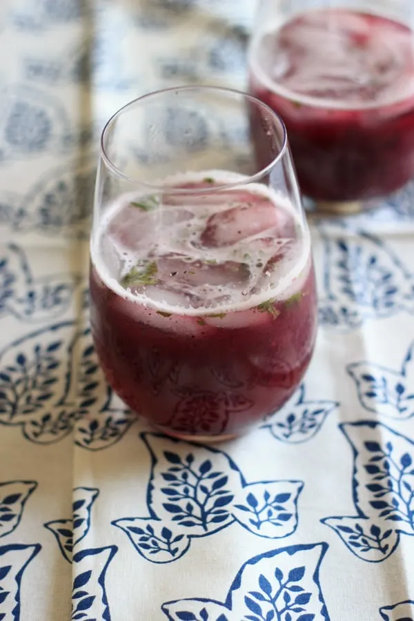 Blueberry mint lemonade in clear glass on blue and white cloth