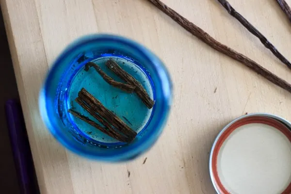 view from the top: blue mason jar with sliced vanilla beans and adding vodka to make extract