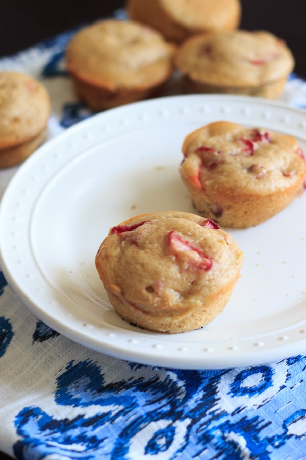 Two Strawberry rhubarb muffins on white plate with more in background