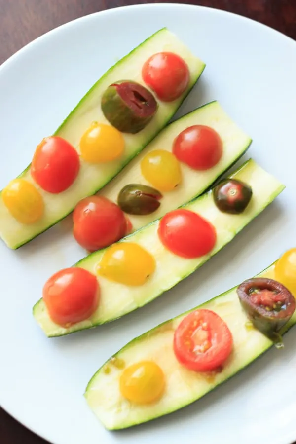 two zucchinis cut in half for quick and easy zucchini boats, with sliced heirloom tomatoes on top