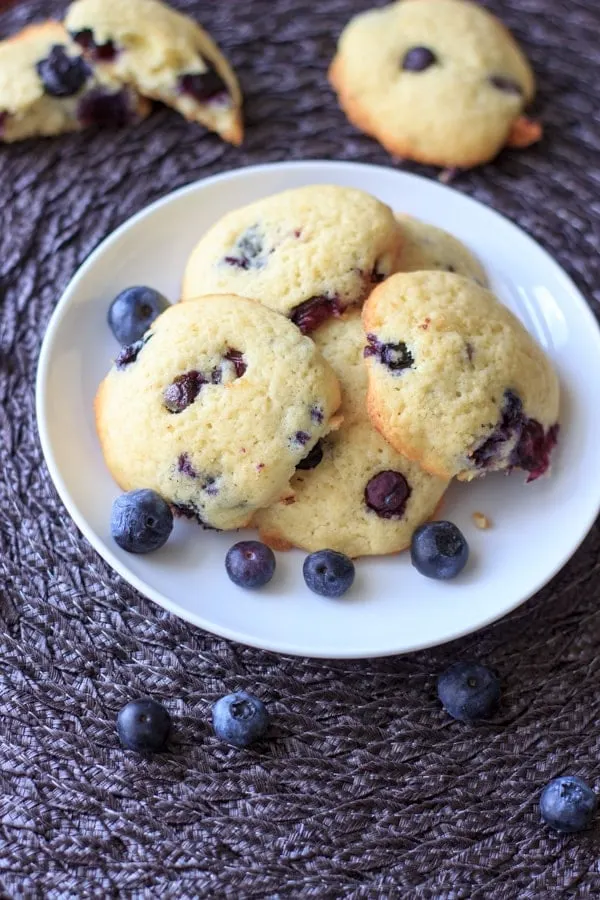 Lemon blueberry cookies piled on white plate and blue placemat