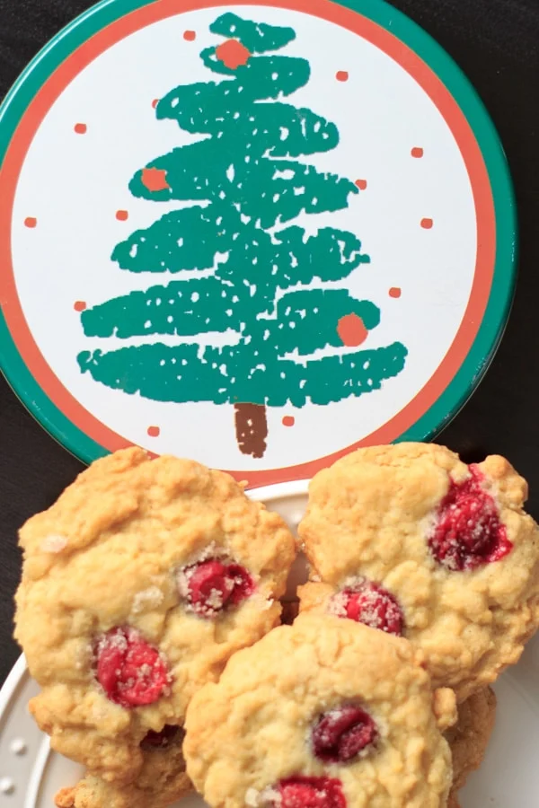 Sugared cranberry cookies next to a cookie tin with a christmas tree design