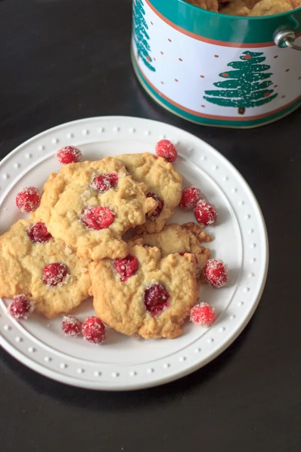 Sugared cranberry cookies on white polka dot plate with christmas tree design tin in background
