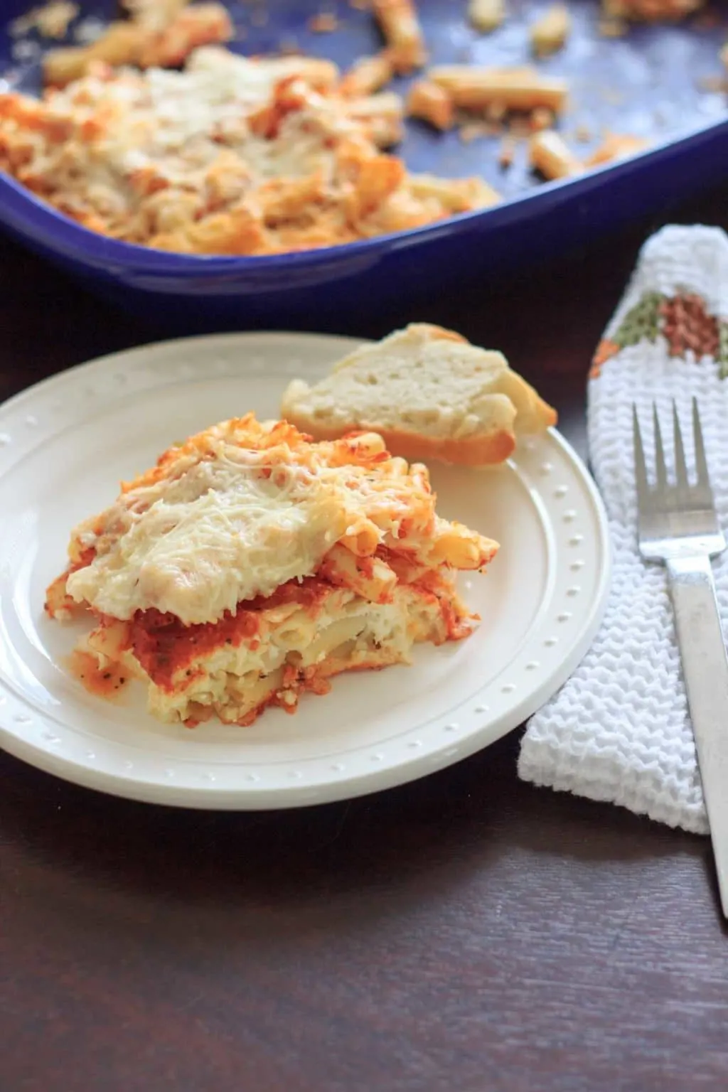 small portion of grandma's baked ziti on white plate with remaining casserole in background