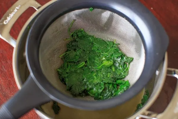 straining excess water out of the sautéed spinach.