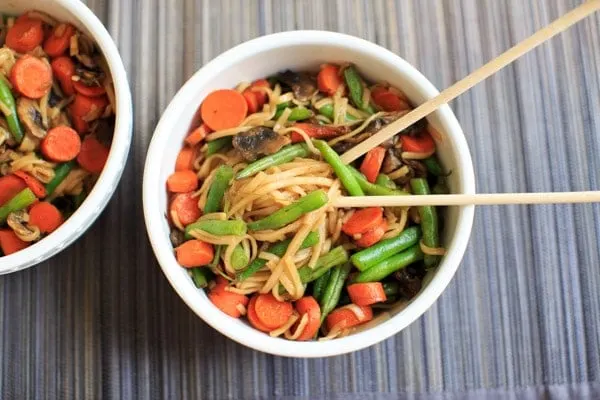 Veggie Lo Mein with mushrooms, green beans and carrots in while bowl with chopsticks.