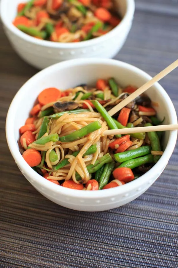 Veggie Lo Mein with mushrooms, green beans and carrots in while bowl with chopsticks.