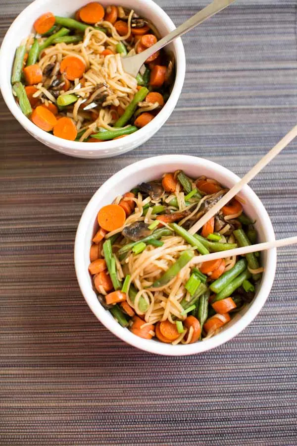 Veggie Lo Mein with mushrooms, green beans and carrots in while bowl with chopsticks.