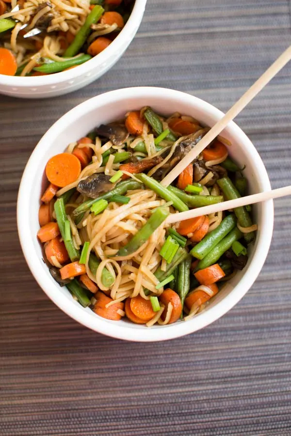 Veggie Lo Mein with mushrooms, green beans and carrots in while bowl with chopsticks.