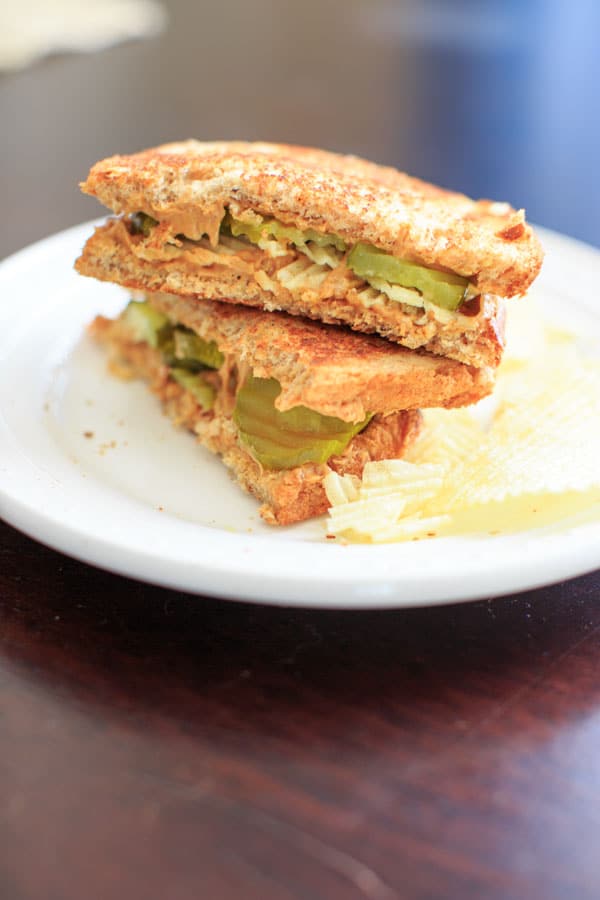 peanut butter and pickles and chips sandwich sliced in half on white plate