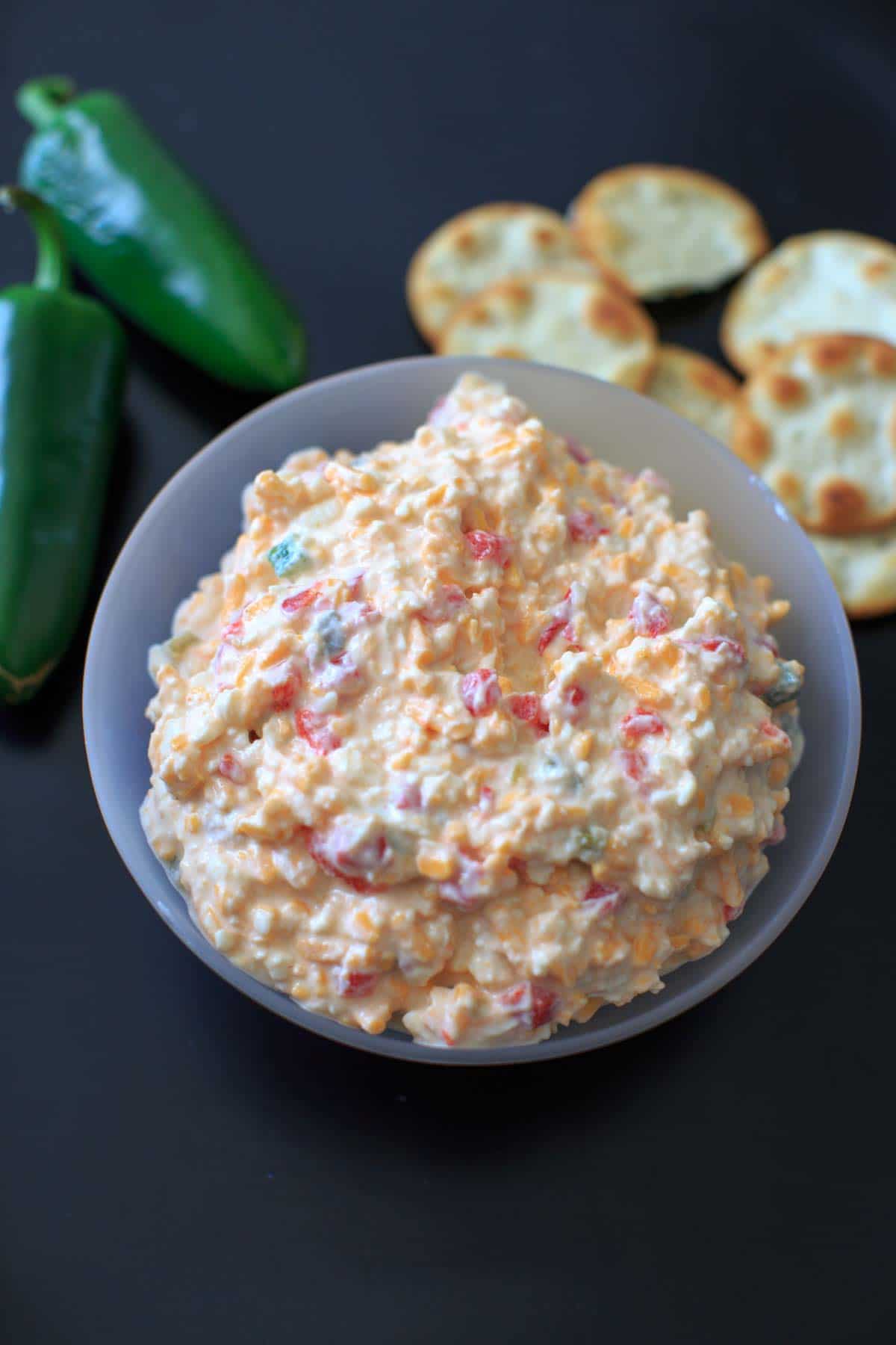 jalapeno pimento cheese in clear bowl with crackers and whole jalapeno in the background