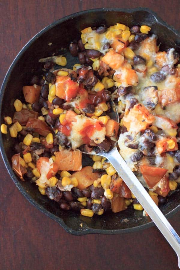 Butternut Squash and Veggie Bake in skillet with a serving spoon and a little hot sauce added