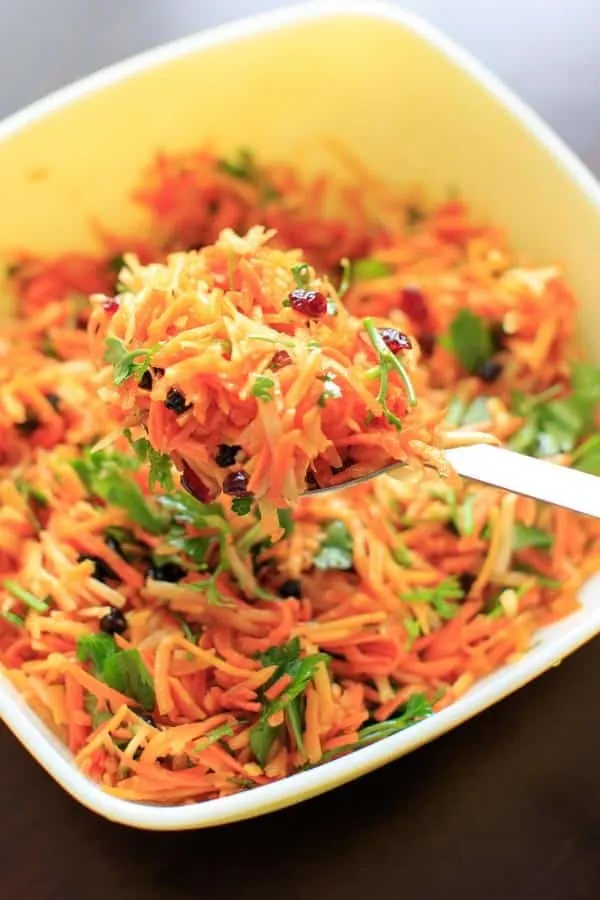 serving spoon scooping a serving of shredded carrot salad from serving bowl