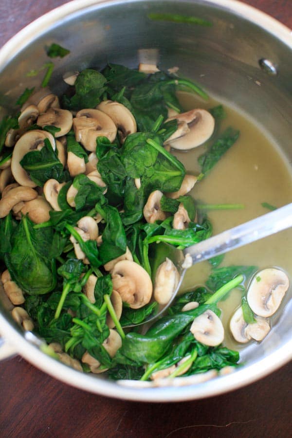 cooking down spinach leaves and mushrooms in pot
