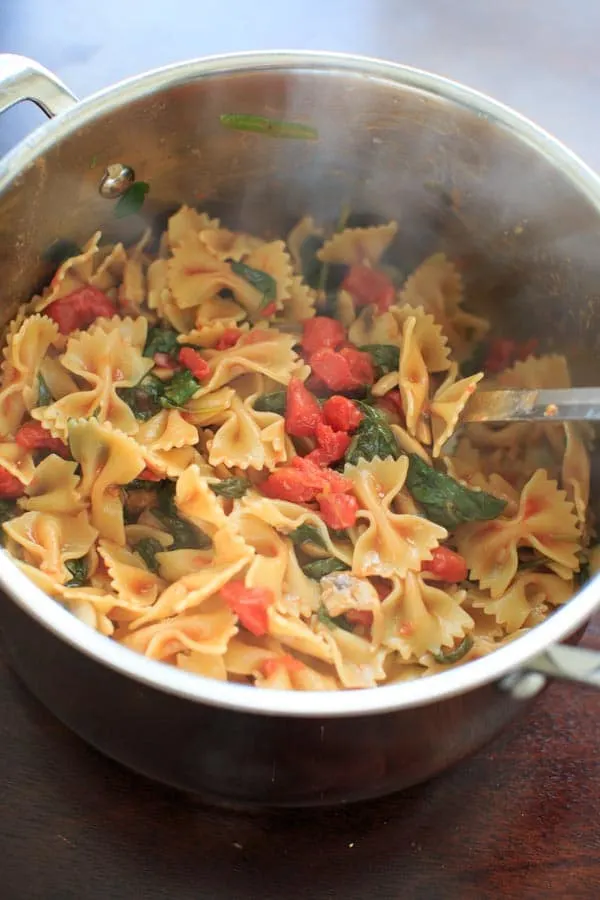 mixing the bowtie pasta in with the veggies in pot