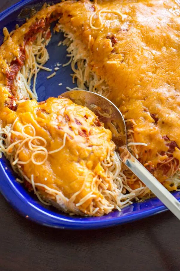 Vegetarian Million Dollar Spaghetti with cheddar cheese, spooning out of the casserole dish