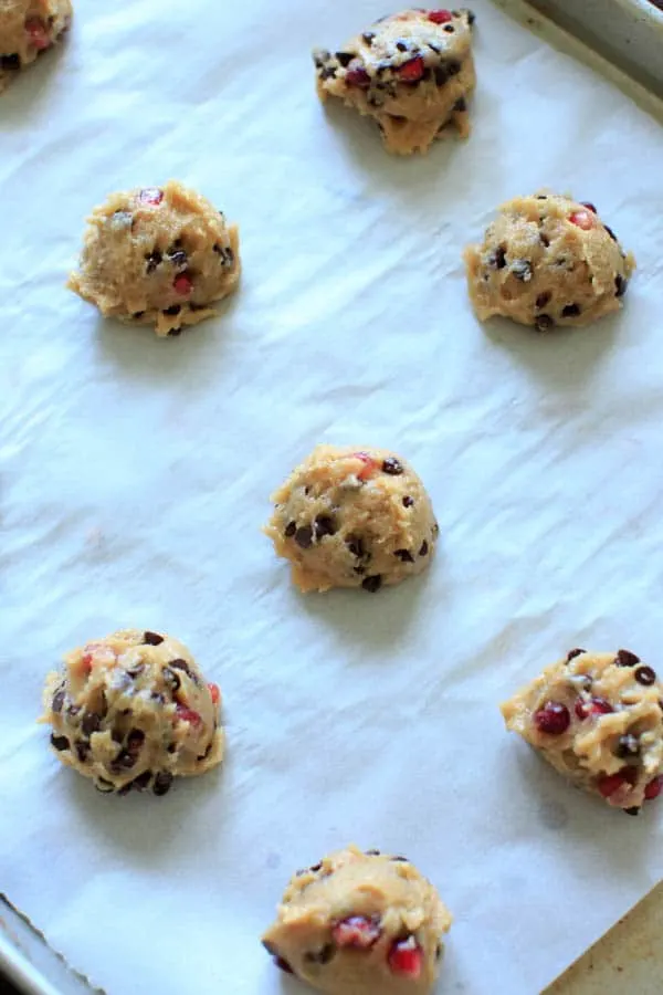 chocolate chip cookie dough with pomegranate seeds scooped into balls on baking sheet