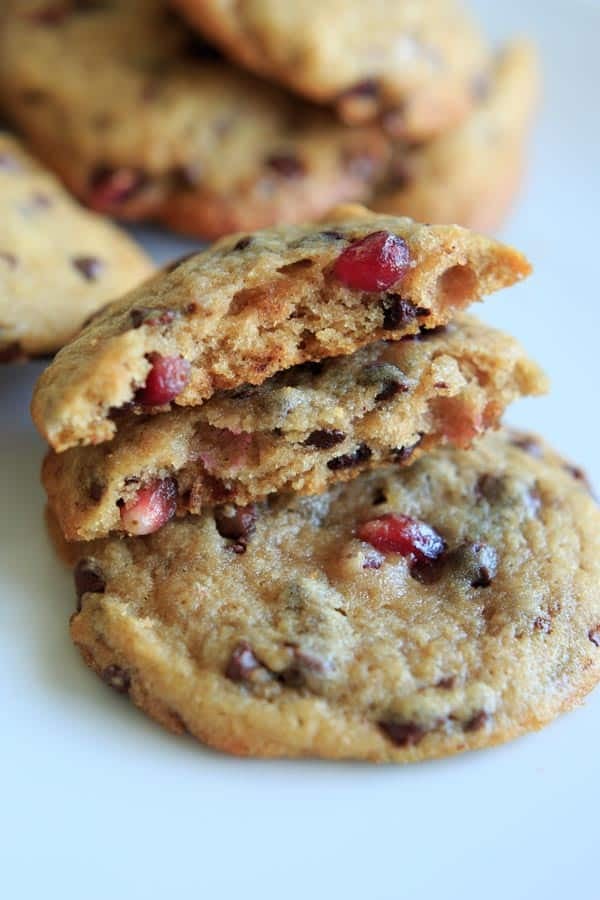 Chocolate Chip Cookies with Pomegranate Seeds stacked on top of one another, with two broken in half to see the inside