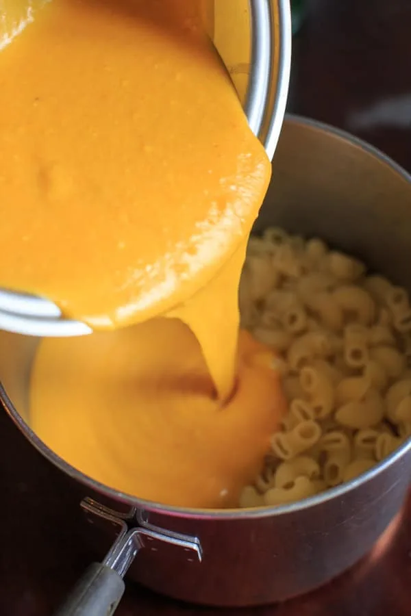 pouring the cheddar pumpkin sauce over macaroni