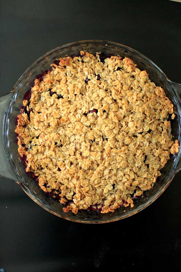 baked blueberry crisp on clear baking dish on black table