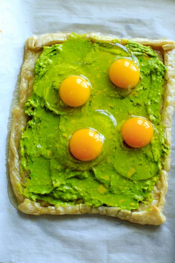 baked puff pastry dough sheet with mashed avocado as base and 4 cracked raw eggs on top 