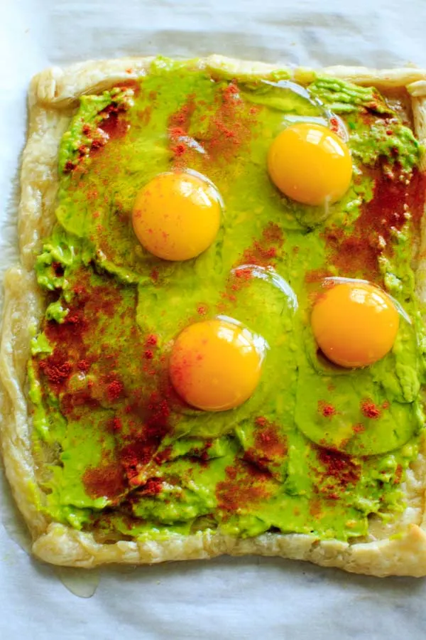 baked puff pastry dough sheet with mashed avocado as base and 4 cracked raw eggs on top and sprinkled with paprika