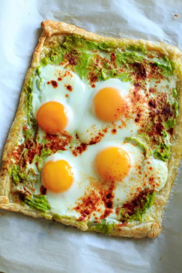 baked puff pastry dough sheet with mashed avocado as base and 4 eggs on top and sprinkled with paprika