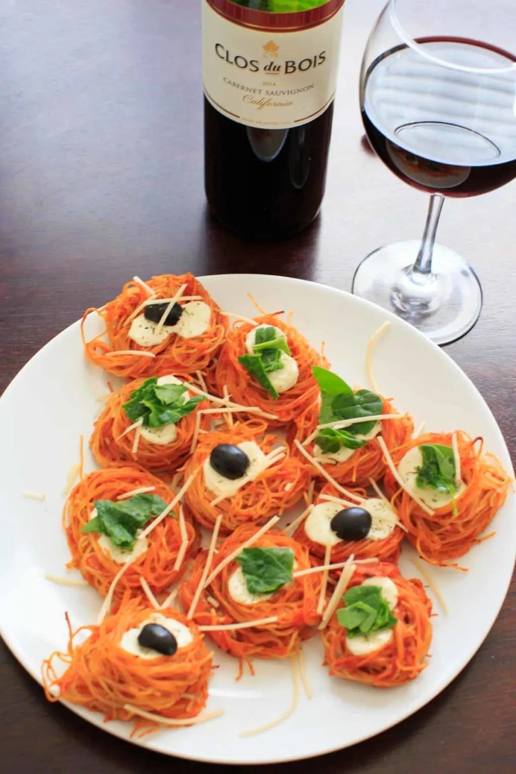 angel hair nests on white plate shaped like a tree with basil leaves and olives on top