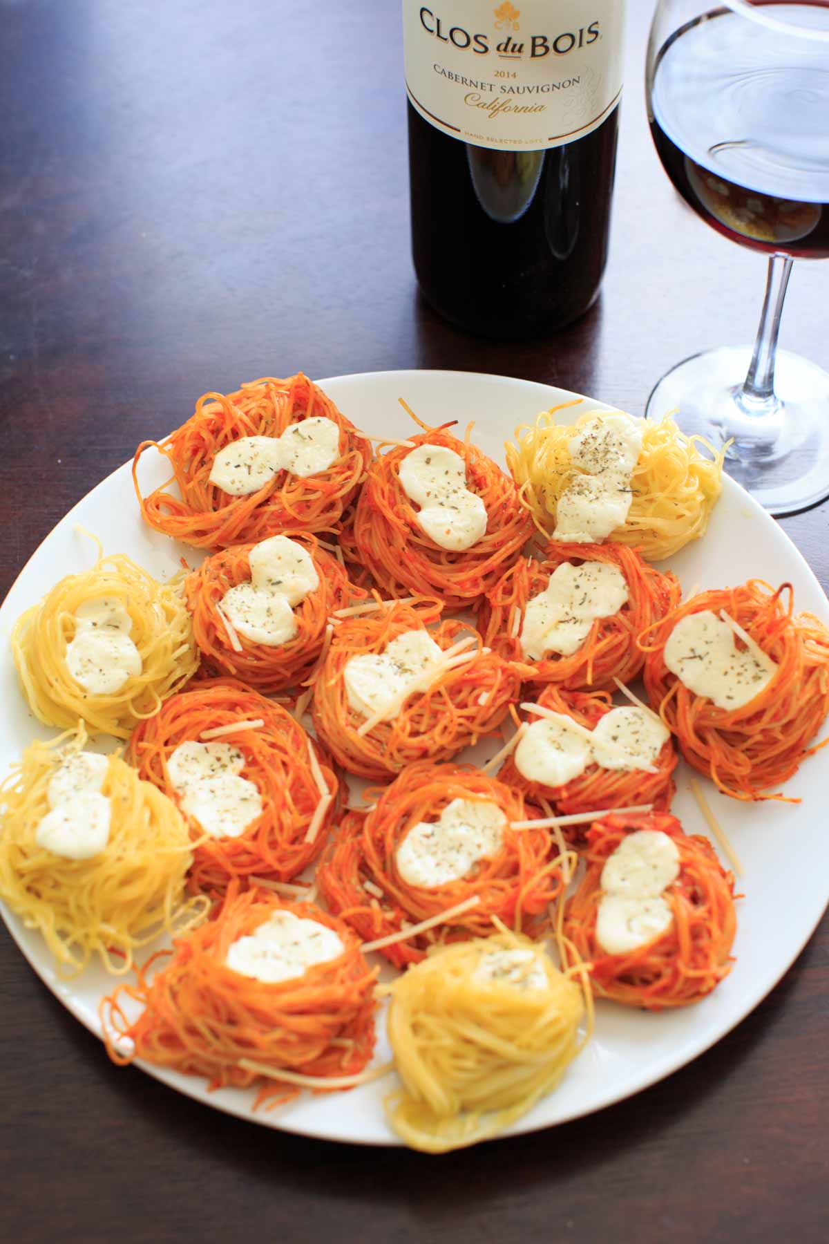 baked spaghetti nests with cheese on top, on white plate with glass of red wine to side of plate