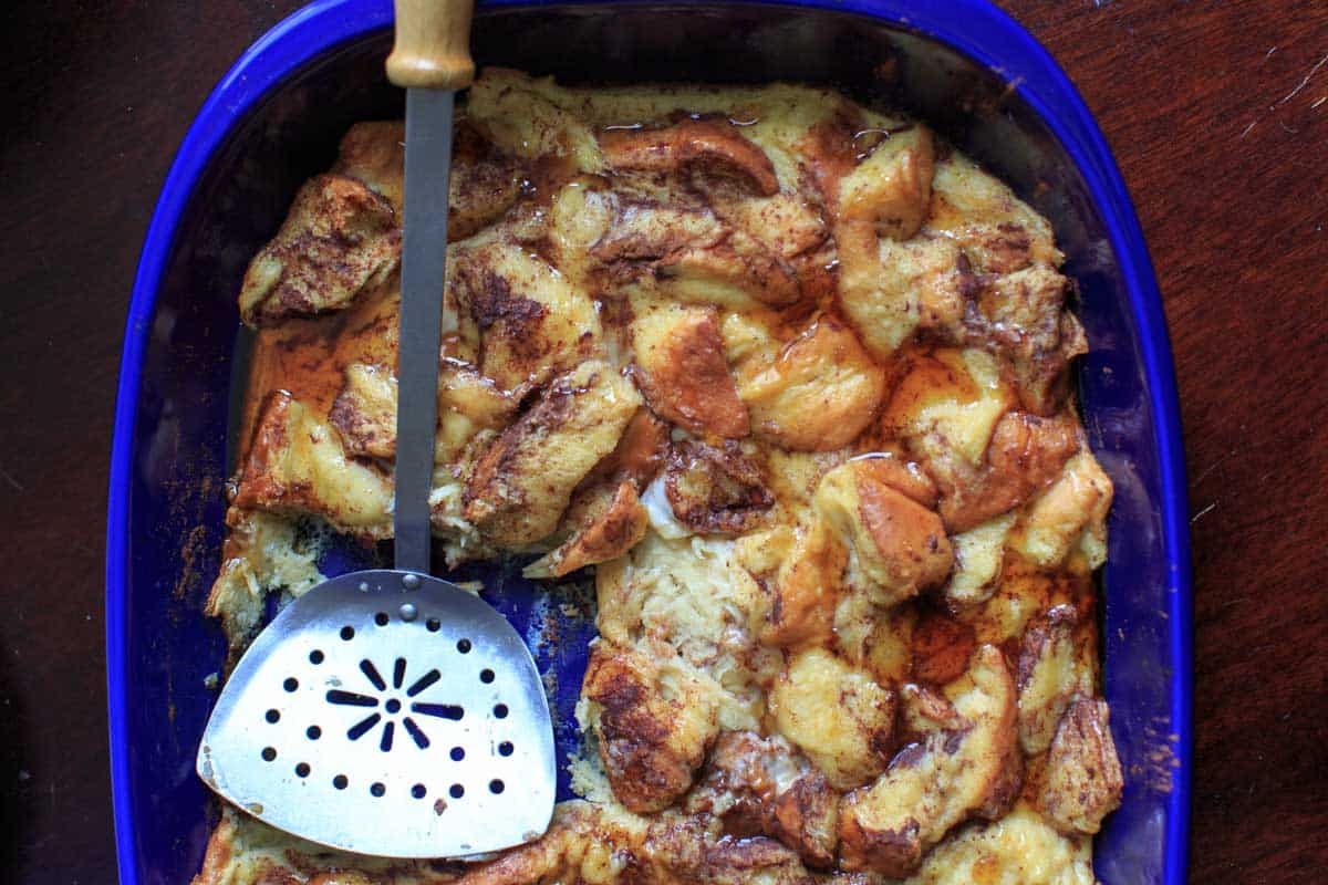 spatula resting in baking pan with one portion taken out of overnight french toast casserole