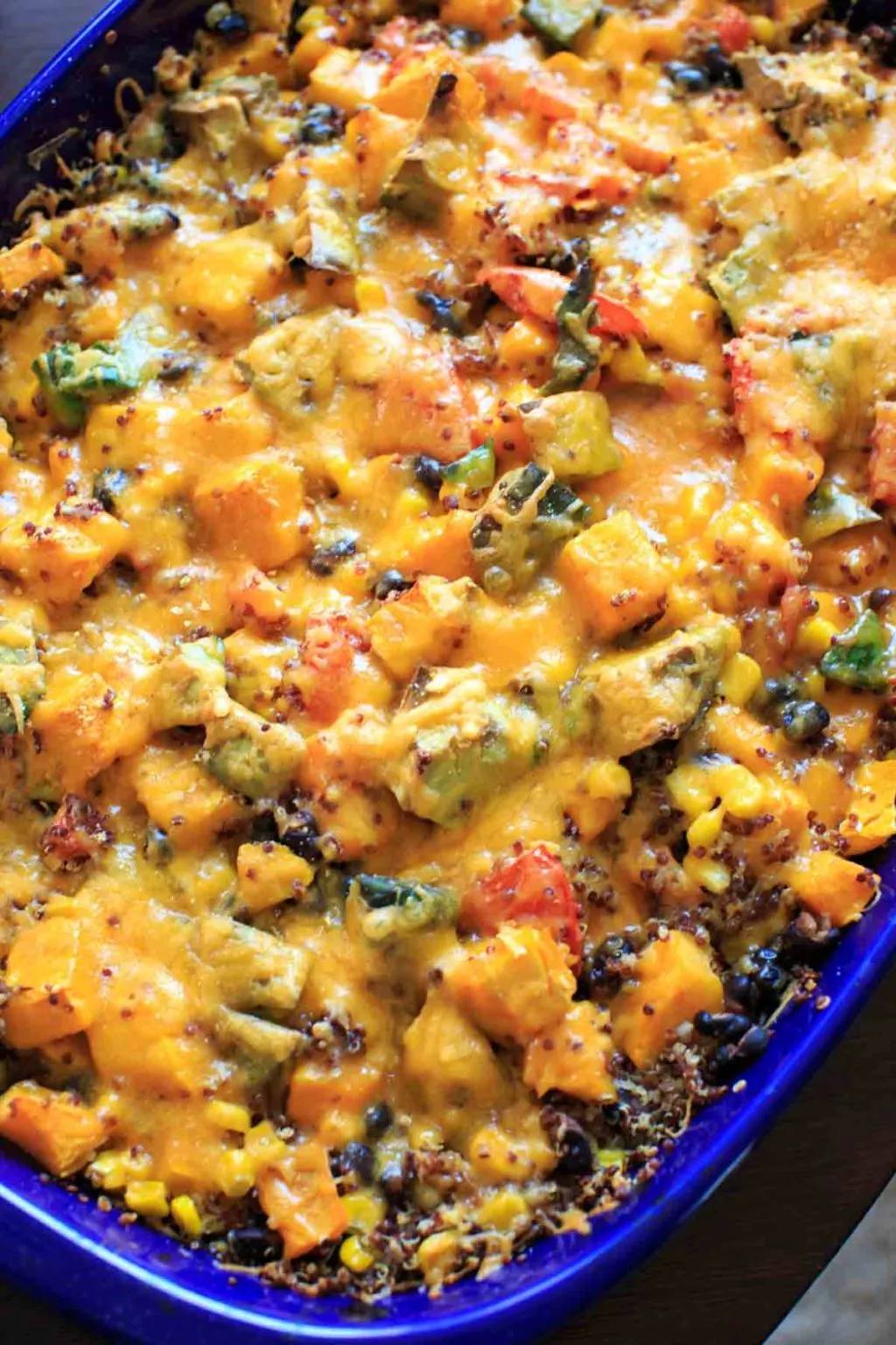 Butternut squash and other vegetables mixed together with quinoa in casserole pan topped with cheese