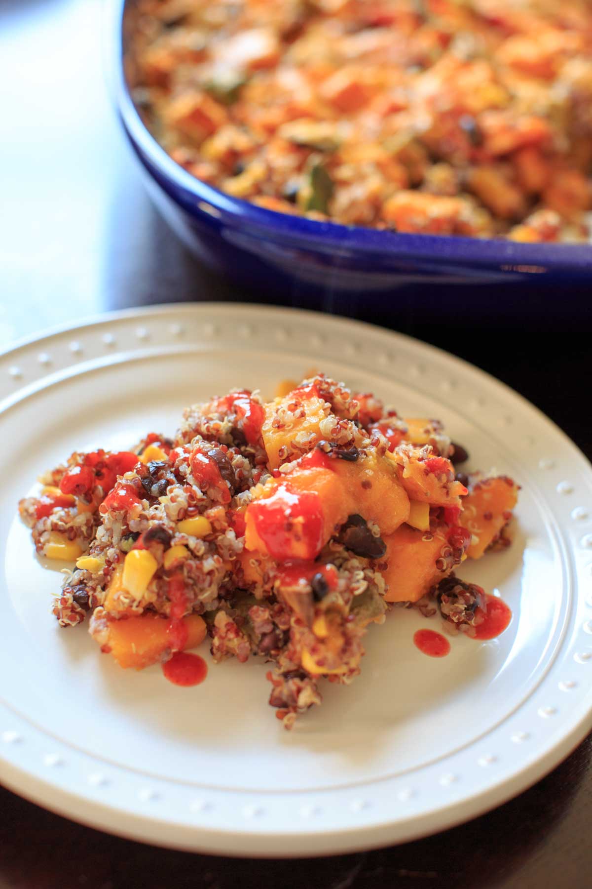 a portion of butternut squash quinoa casserole on white plate topped with hot sauce