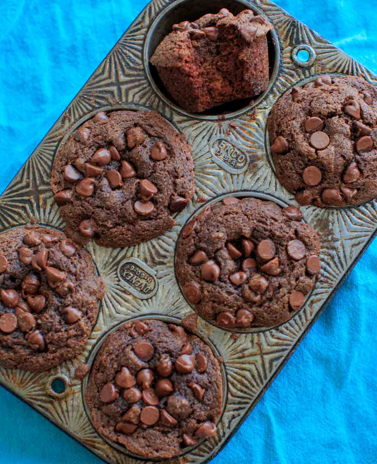 6 double chocolate coconut flour muffins in muffin pan, one turned over with bite out of it