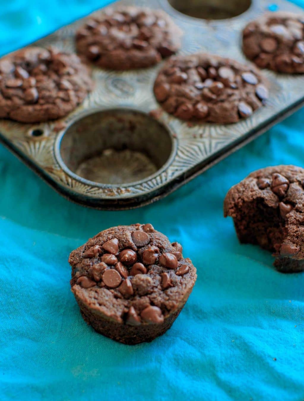 close up of muffin next to one half eaten one and muffin tin in background on blue cloth