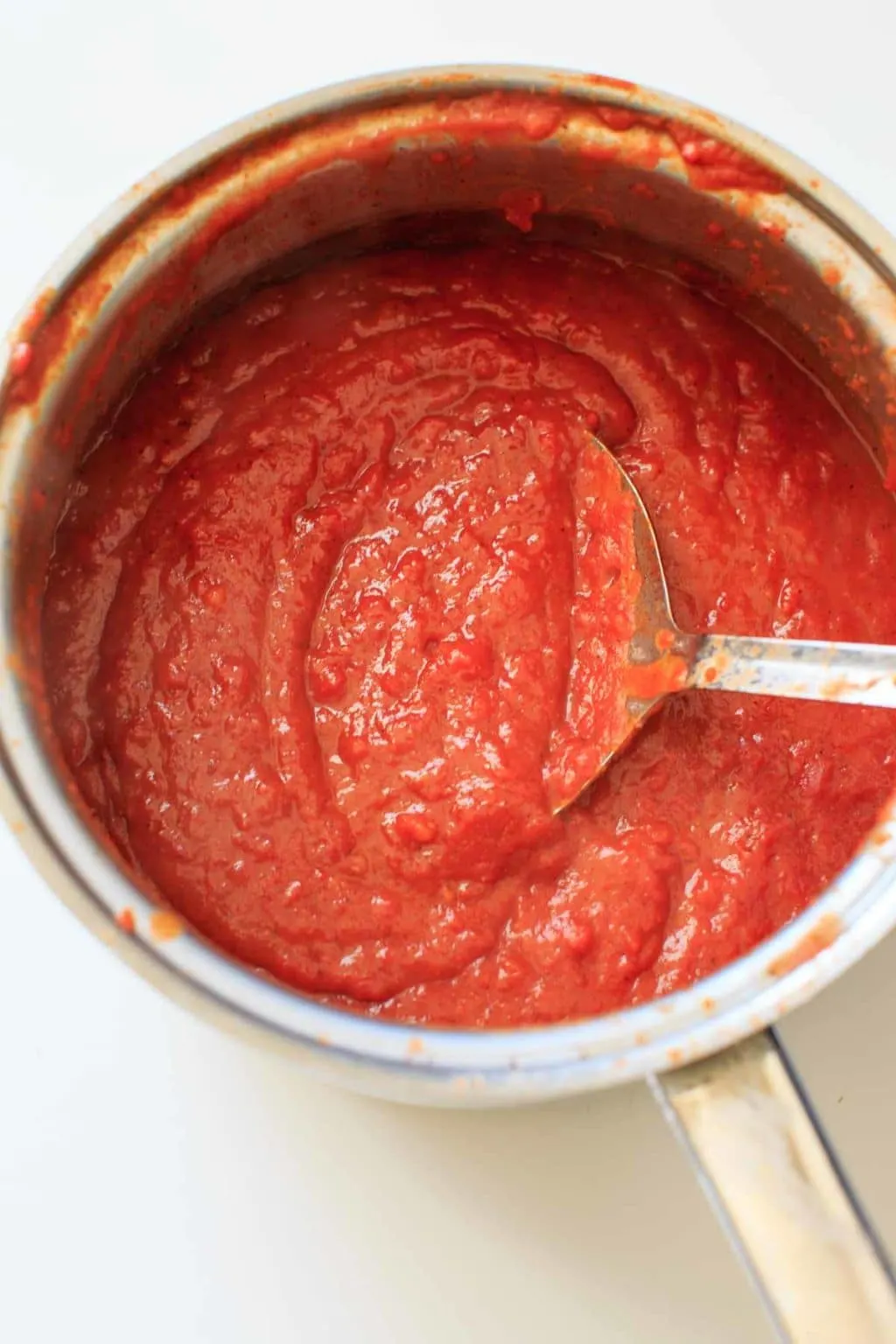 Homemade Enchilada Sauce in pot stirring with large sauce spoon