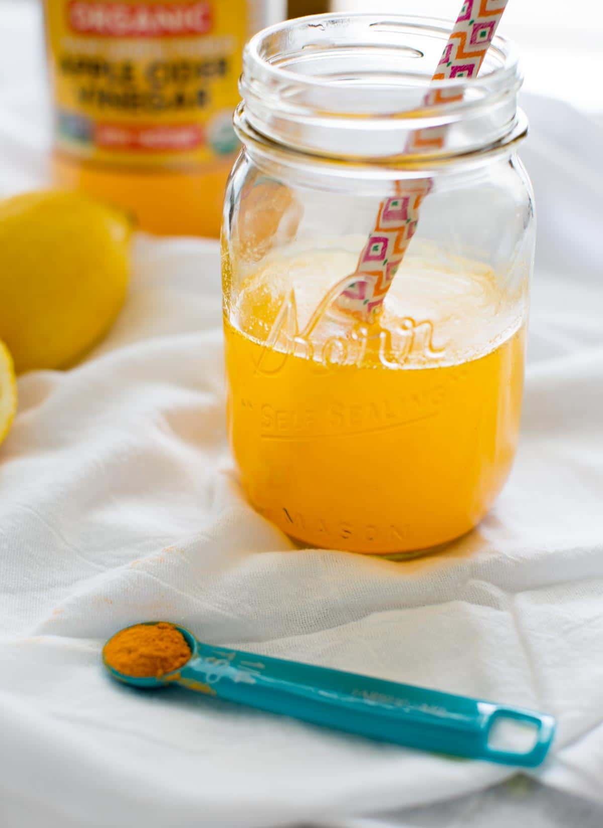 turmeric detox drink in clear mason jar with straw and apple cider vinegar jar and lemon in background