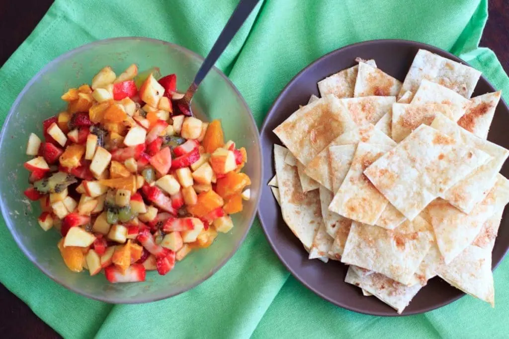 fruit salsa in a clear bowl next to baked cinnamon sugar chips on green cloth